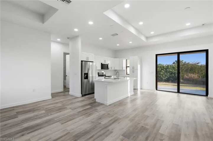 Kitchen with an island with sink, stainless steel appliances, open floor plan, white cabinets, and a raised ceiling