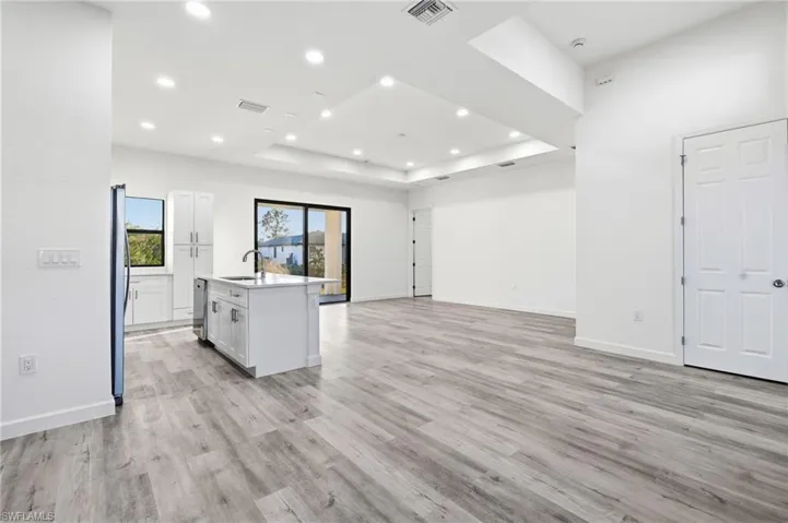 Kitchen with a center island with sink, open floor plan, white cabinets, a raised ceiling, and recessed lighting