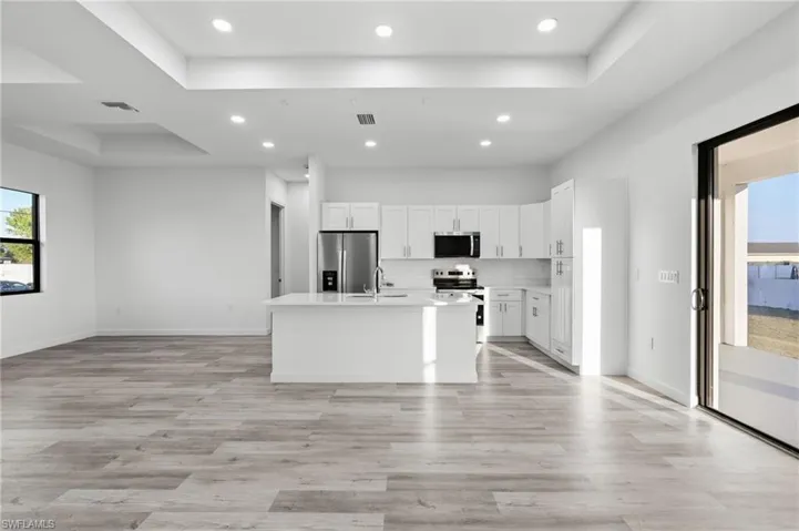 Kitchen featuring healthy amount of natural light, white cabinetry, open floor plan, a kitchen island with sink, and a raised ceiling