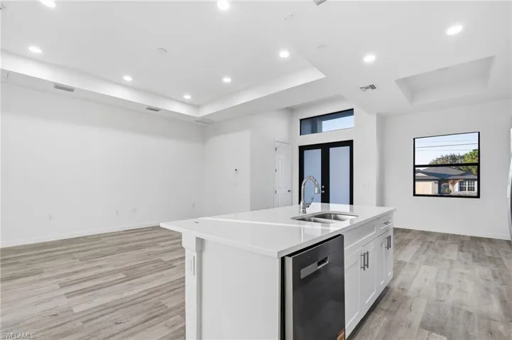 Kitchen featuring a tray ceiling, dishwasher, recessed lighting, white cabinets, and a center island with sink