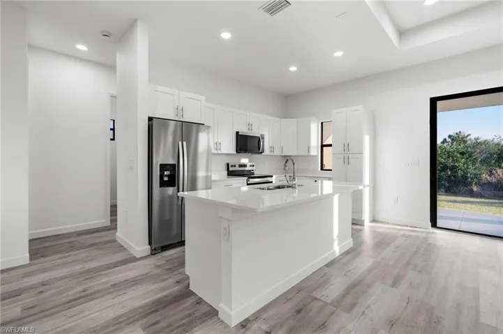Kitchen with stainless steel appliances, white cabinetry, a center island with sink, light stone countertops, and light wood finished floors