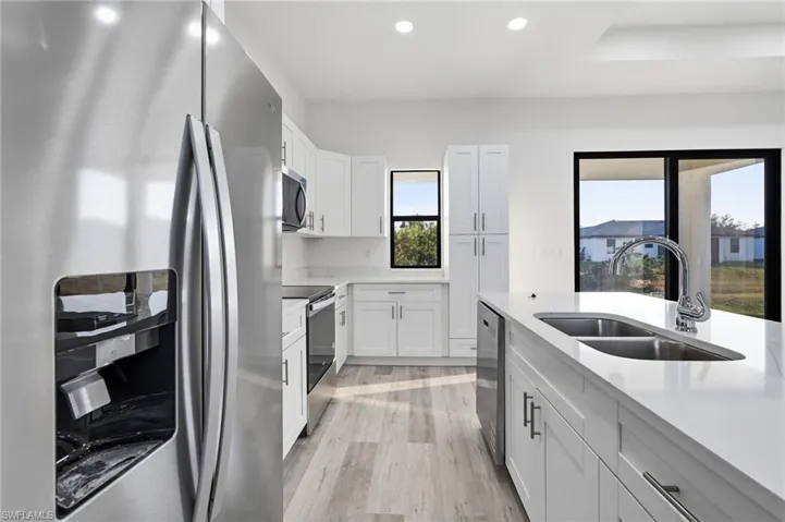 Kitchen featuring stainless steel appliances, white cabinetry, recessed lighting, light stone counters, and light wood-style floors