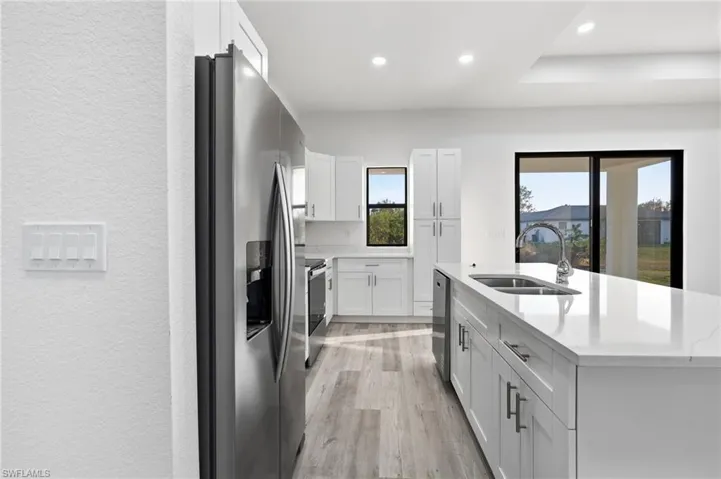 Kitchen featuring a textured wall, stainless steel appliances, white cabinets, an island with sink, and light stone counters