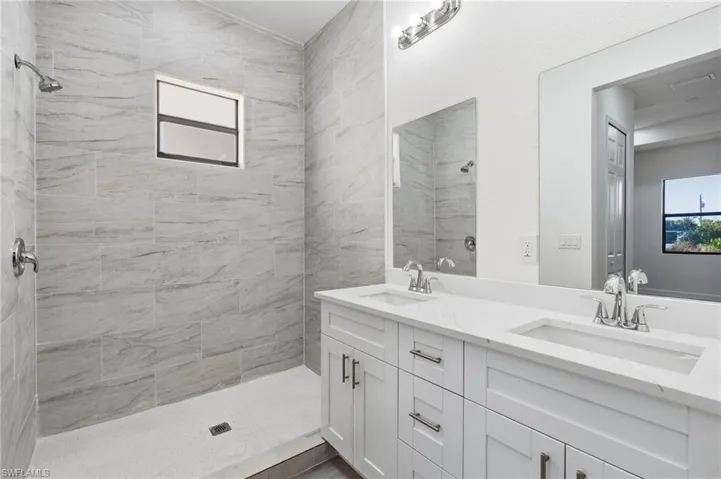 Full bath featuring healthy amount of natural light, double vanity, and a shower stall