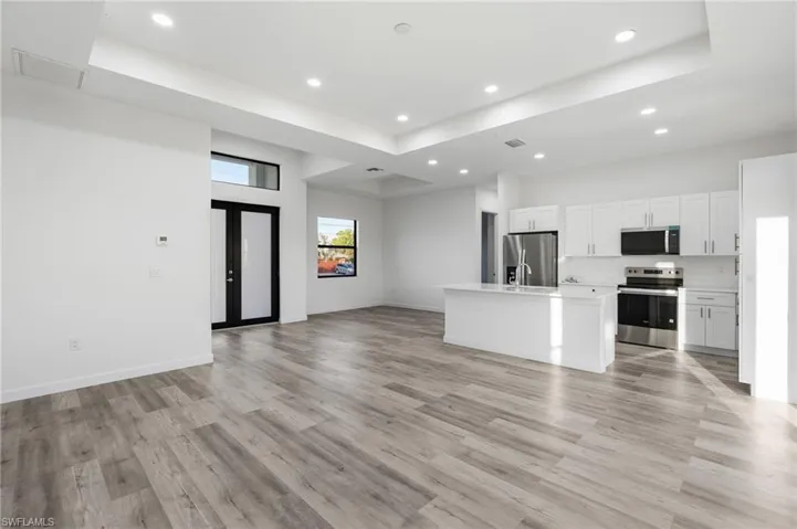 Kitchen with open floor plan, a center island with sink, white cabinetry, french doors, and stainless steel appliances
