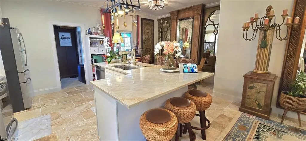 Kitchen featuring a peninsula, light stone finish floors, baseboards, appliances with stainless steel finishes, and a chandelier