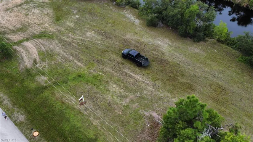 Expansive grassy lot featuring a water frontage, mature trees, and existing power lines