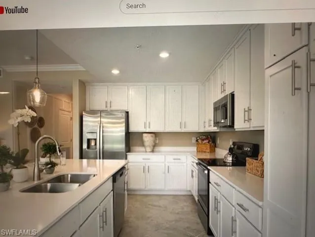 Kitchen with ornamental molding, stainless steel appliances, sink, white cabinetry, and hanging light fixtures