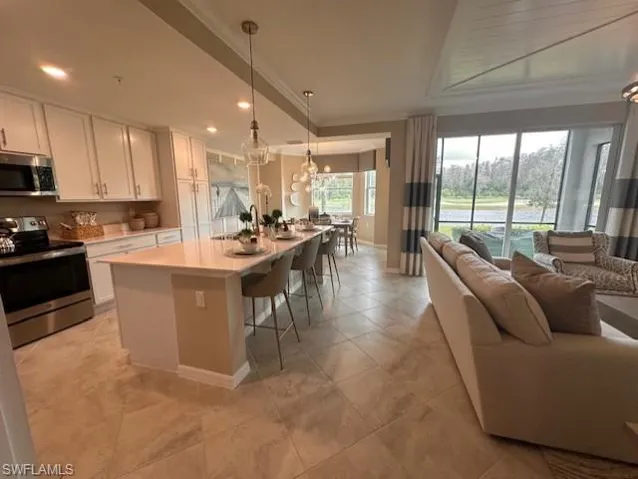 Kitchen featuring a center island with sink, a breakfast bar, white cabinetry, hanging light fixtures, and stainless steel appliances