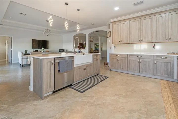 Kitchen featuring light brown cabinetry, crown molding, arched walkways, open floor plan, and stainless steel dishwasher