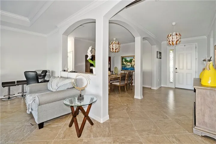 Living room featuring a chandelier, crown molding, arched walkways, and light tile patterned flooring