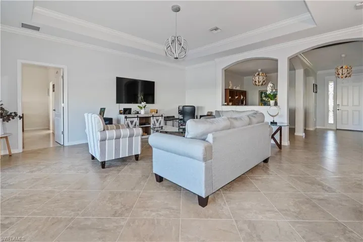 Living room featuring arched walkways, a raised ceiling, a chandelier, and ornamental molding