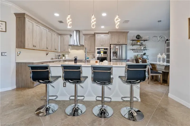 Kitchen with pendant lighting, crown molding, a breakfast bar, a kitchen island with sink, and appliances with stainless steel finishes