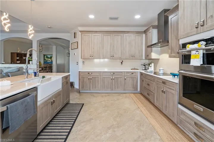 Kitchen with stainless steel appliances, wall chimney range hood, pendant lighting, ornamental molding, and open floor plan