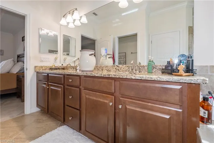Ensuite bathroom featuring crown molding, double vanity, and light tile patterned floors