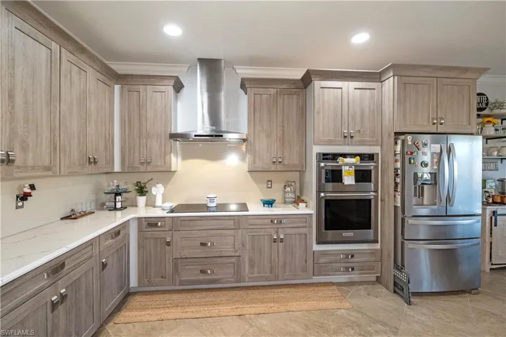 Kitchen with stainless steel appliances, wall chimney exhaust hood, light stone countertops, and recessed lighting