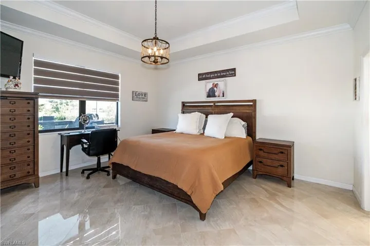 Bedroom with ornamental molding, a tray ceiling, a desk, and a chandelier