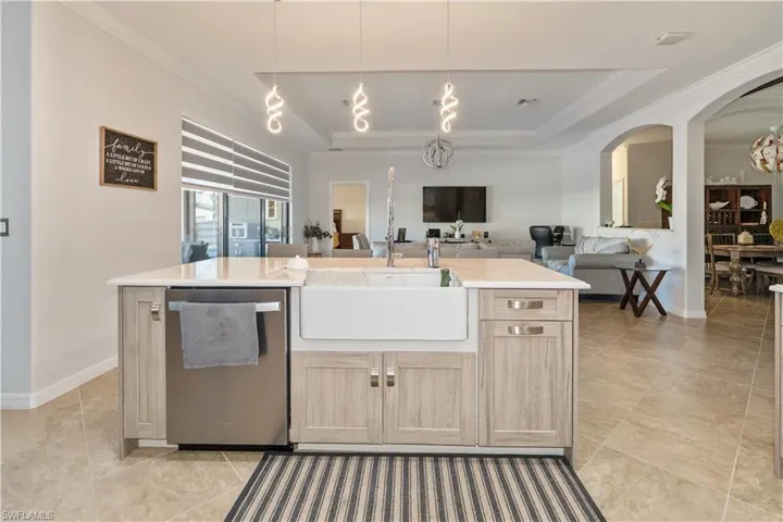 Kitchen with light brown cabinets, stainless steel dishwasher, decorative light fixtures, an island with sink, and arched walkways