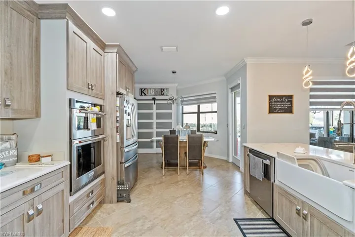 Kitchen with a chandelier, light brown cabinets, stainless steel appliances, decorative light fixtures, and light stone countertops