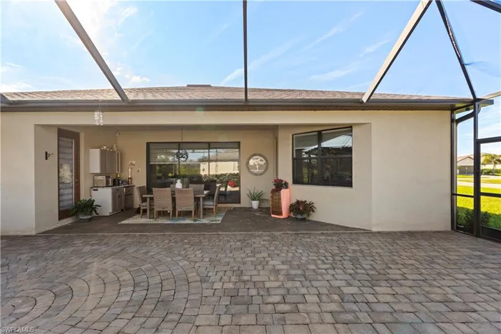 Rear view of house with stucco siding, glass enclosure, a sunroom, outdoor dining space, and a patio
