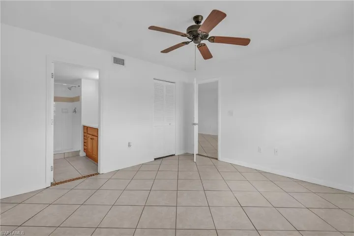 Unfurnished bedroom with light tile patterned floors, ensuite bathroom, and a ceiling fan