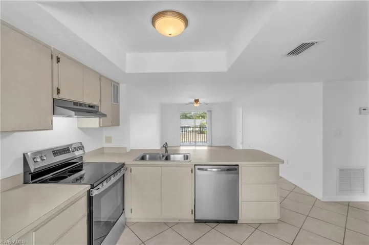Kitchen featuring stainless steel appliances, a peninsula, light countertops, ceiling fan, and a raised ceiling
