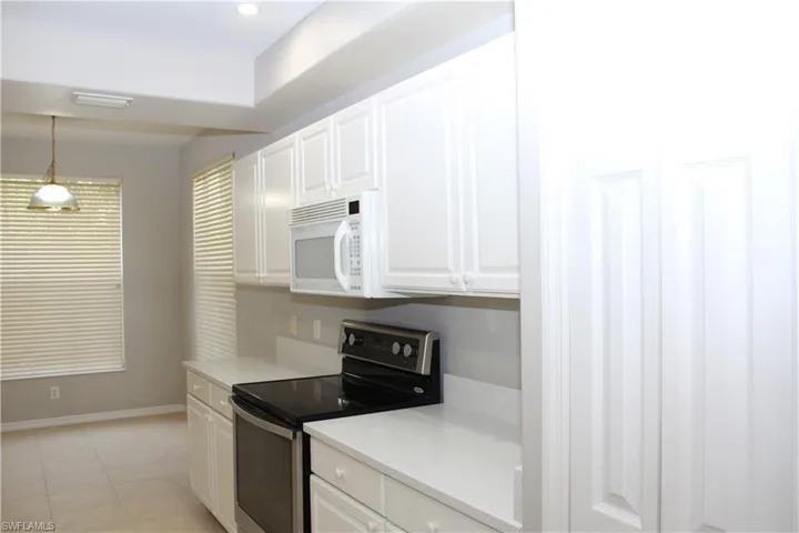 Kitchen with white cabinets, stainless steel electric stove, hanging light fixtures, and light tile patterned floors