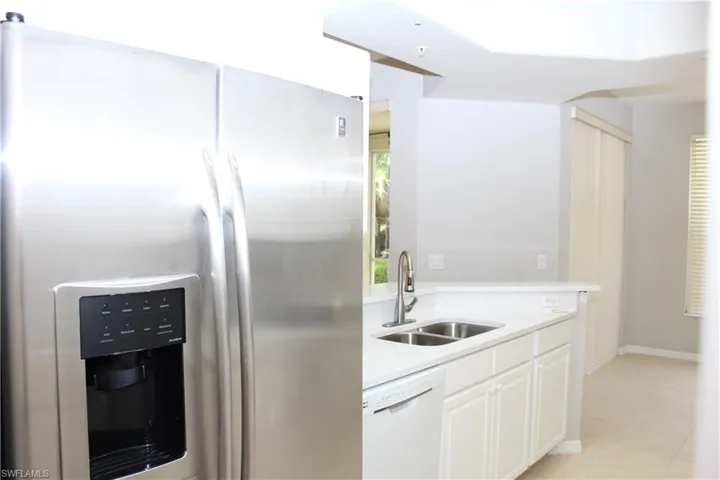 Kitchen featuring light tile patterned flooring, stainless steel refrigerator with ice dispenser, dishwasher, white cabinets, and sink