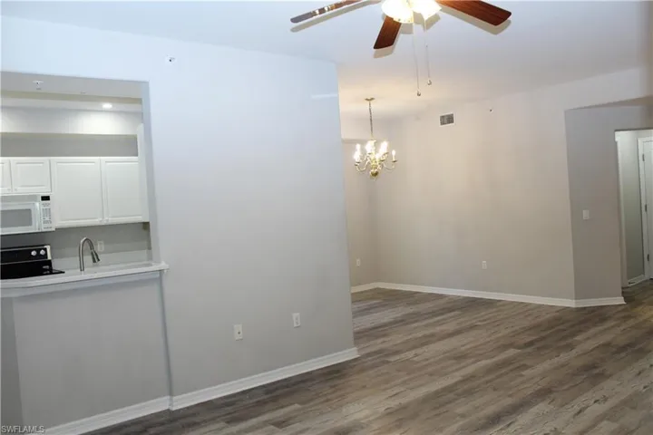 Spare room featuring ceiling fan with notable chandelier and wood-type flooring