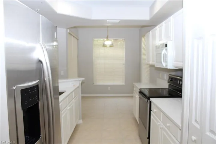 Kitchen featuring light tile patterned flooring, stainless steel refrigerator with ice dispenser, white cabinets, pendant lighting, and range with electric stovetop