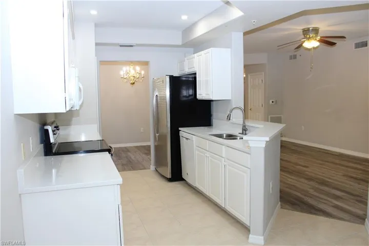 Kitchen with light tile patterned flooring, white appliances, sink, and white cabinets