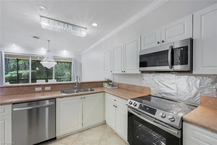 Kitchen featuring stainless steel appliances, white cabinetry, ornamental molding, light countertops, and recessed lighting