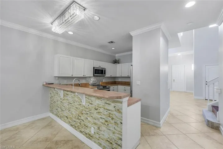 Kitchen featuring recessed lighting, crown molding, light tile patterned floors, white cabinetry, and light countertops
