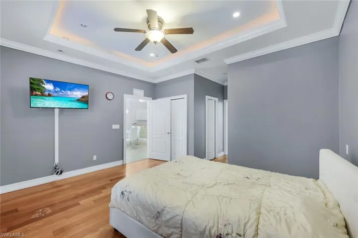 Bedroom featuring a raised ceiling, light wood finished floors, two closets, crown molding, and ceiling fan