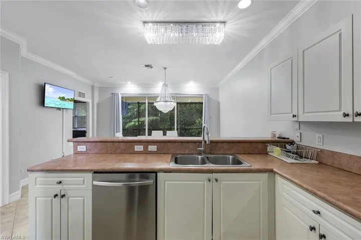 Kitchen featuring a peninsula, stainless steel dishwasher, white cabinetry, hanging light fixtures, and crown molding