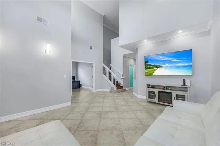 Living area with a towering ceiling, crown molding, stairs, and light tile patterned floors