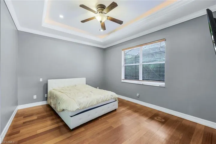 Bedroom with crown molding, a raised ceiling, wood finished floors, and ceiling fan