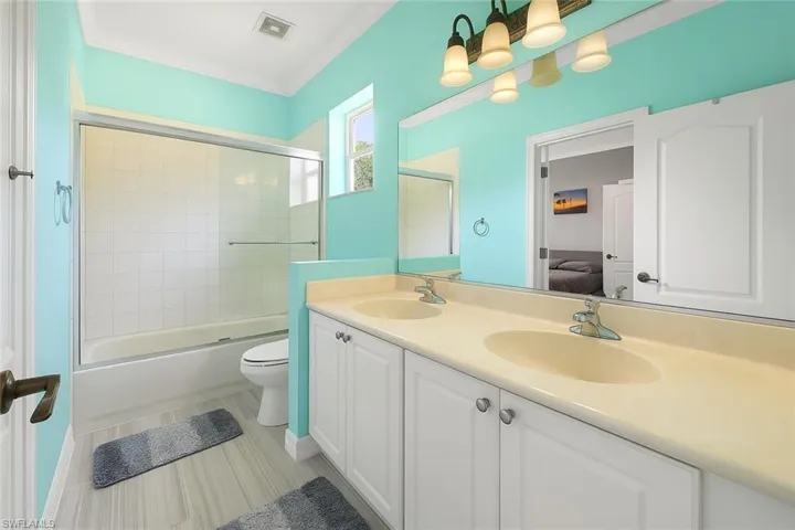 Ensuite bathroom featuring double vanity, combined bath / shower with glass door, and crown molding
