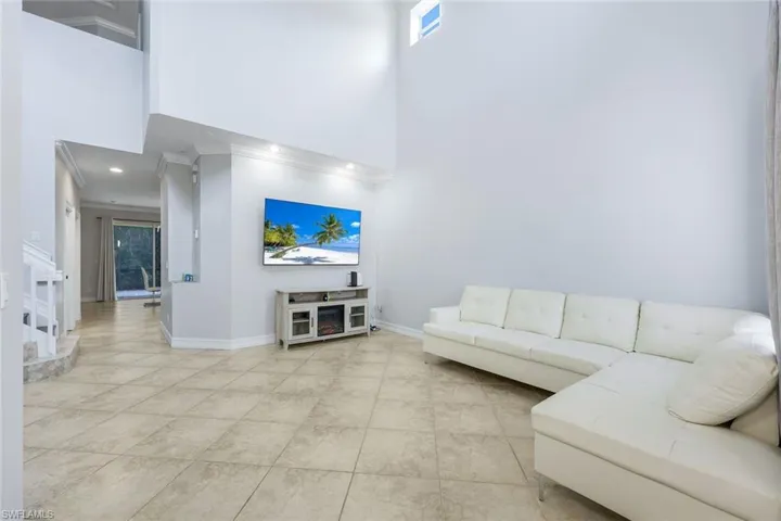 Living room featuring a towering ceiling, light tile patterned floors, and crown molding