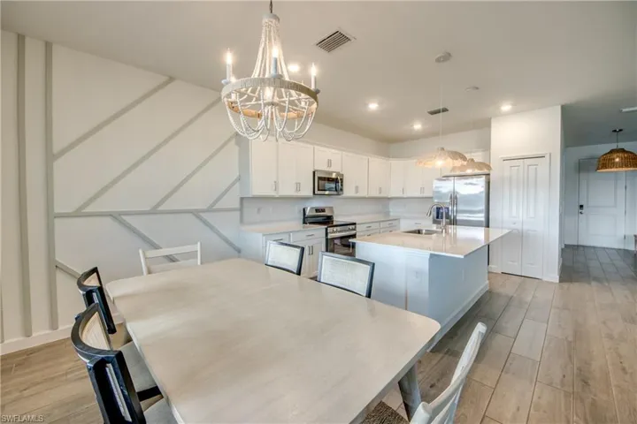 Kitchen featuring white cabinets, a kitchen island with sink, appliances with stainless steel finishes, light wood finished floors, and decorative light fixtures