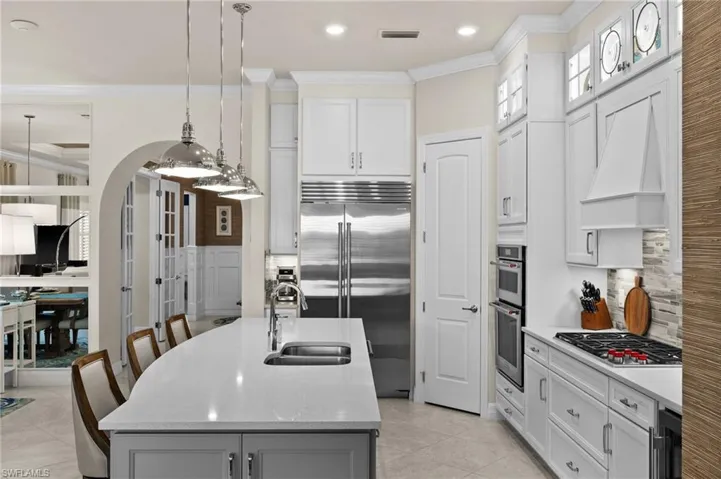 Kitchen featuring stainless steel appliances, a kitchen island with sink, sink, white cabinets, and hanging light fixtures