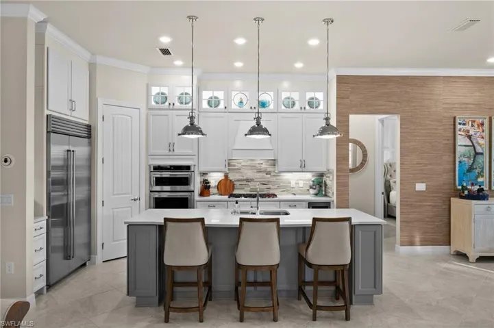 Kitchen featuring pendant lighting, white cabinets, a center island with sink, tasteful backsplash, and stainless steel appliances