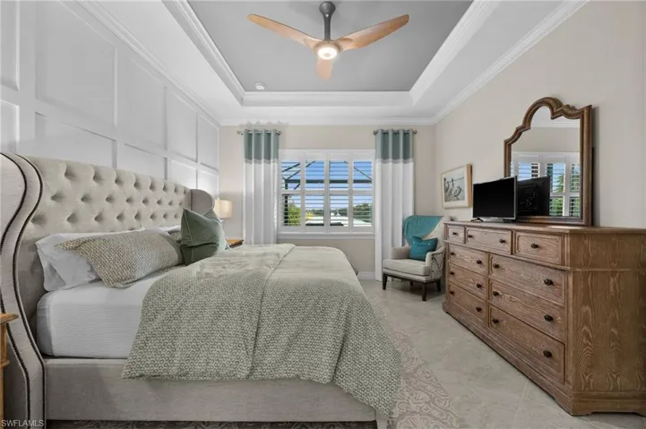 Bedroom with a raised ceiling, ceiling fan, and ornamental molding