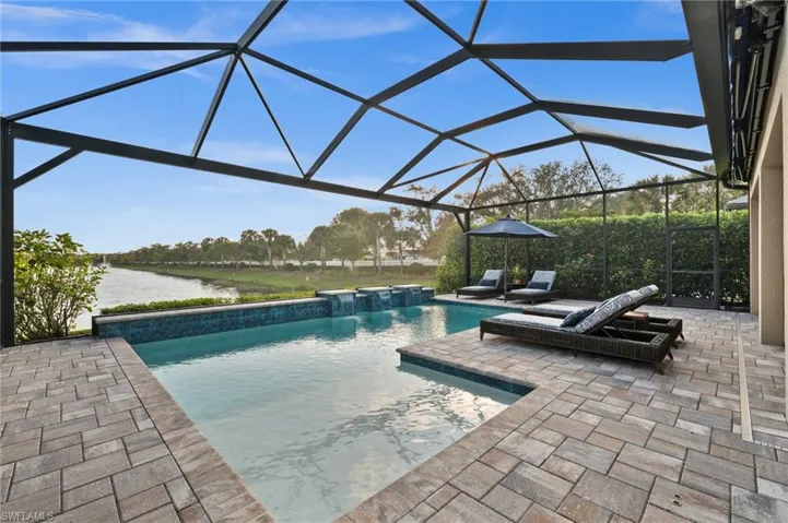 View of pool featuring glass enclosure, a jacuzzi, pool water feature, a patio area, and a water view