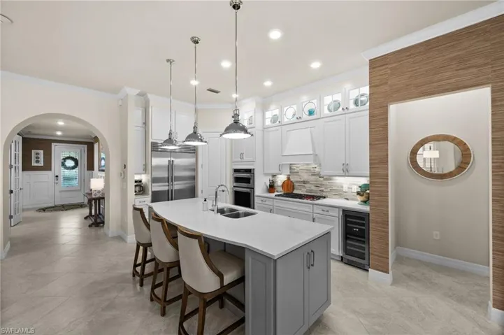 Kitchen featuring premium range hood, crown molding, white cabinets, wine cooler, and an island with sink