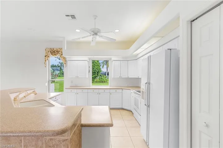 Kitchen featuring white appliances, a ceiling fan, white cabinets, light tile patterned flooring, and recessed lighting