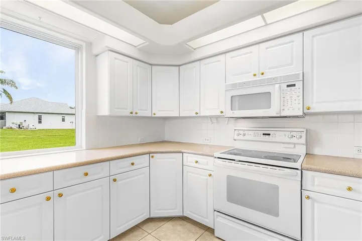 Kitchen featuring white appliances, white cabinets, tasteful backsplash, and light countertops