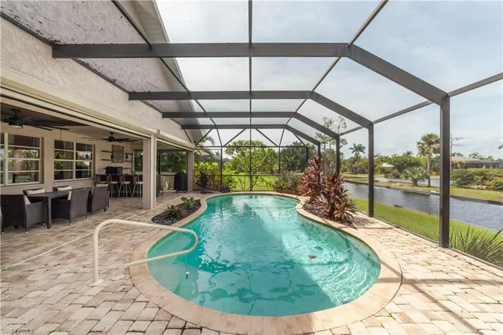 View of pool featuring glass enclosure, a water view, ceiling fan, and a patio