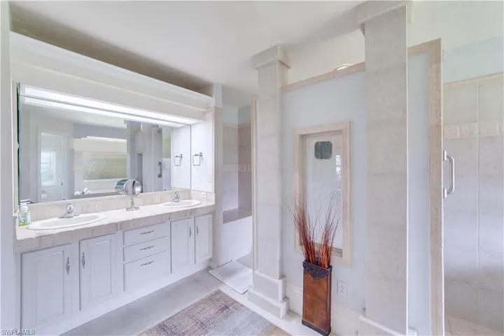 Master Bathroom featuring double sink vanity, decorative columns, tile patterned flooring, and a shower with door