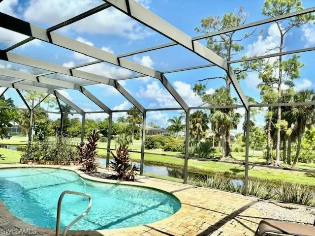 View of swimming pool featuring glass enclosure, a water view, and a patio area